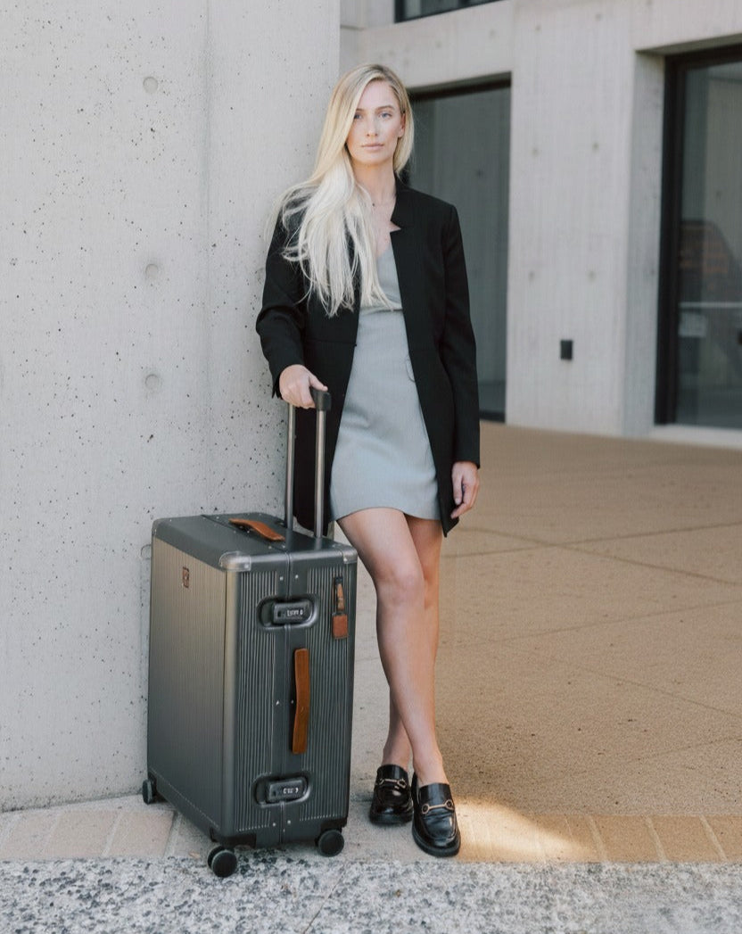 Woman with a suitcase standing against a concrete wall.