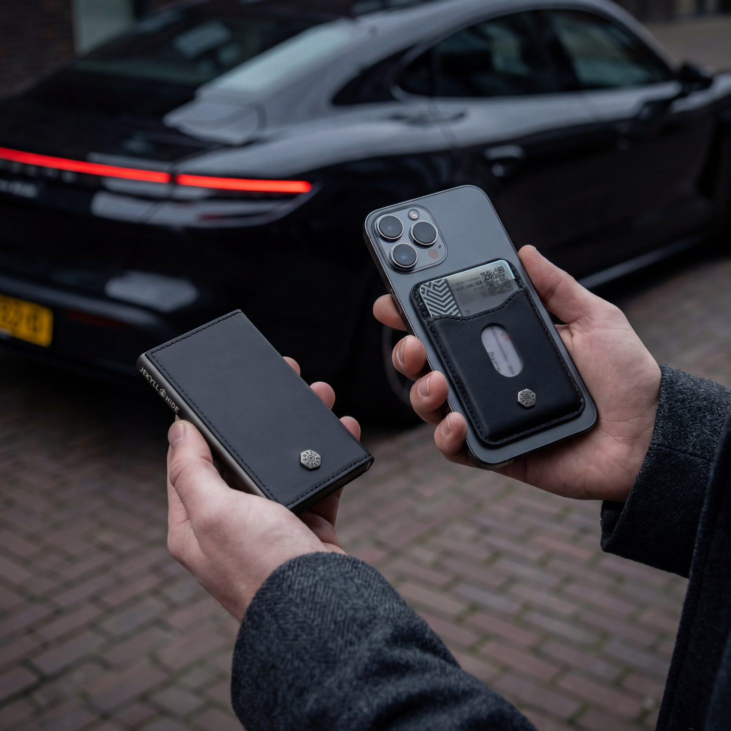 Two hands holding smartphones with a black car in the background
