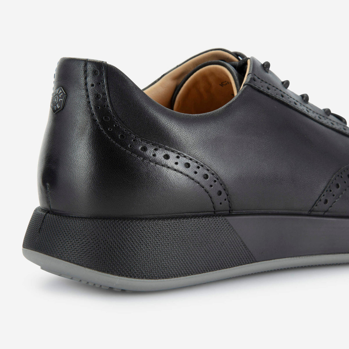 Close-up of the brogue heel detailing and branded rivet on the black Sicily sneaker, Jekyll & Hide